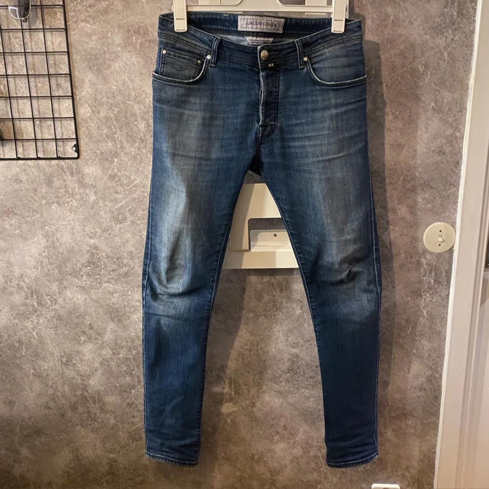 Snygga blå jeans från Jacob Cohen med knappgylf och klassisk femficksdesign. Jeansen har en stilren look med lätt slitna detaljer och en bekväm passform. Nypris 5000. Farkut & Housut.
