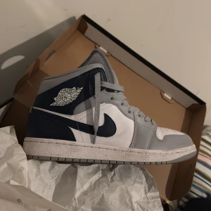 Nike Air Jordans i grått och vitt - Snygga Nike Air Jordans i en stilren kombination av grått, vitt och mörkblått. Skorna har den klassiska Air Jordan-loggan på sidan och snörning framtill. Perfekta för dig som vill ha en sportig och trendig look.