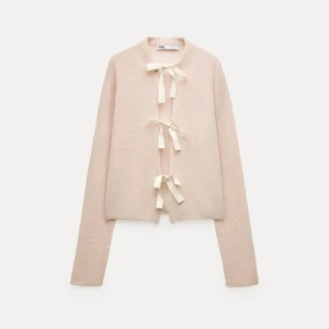 Beige kofta med rosetter från Zara - Säljer en elegant beige kofta från Zara med unika rosettdetaljer framtill. Koftan har långa ärmar och en mjuk, bekväm passform. Perfekt för en stilren look.