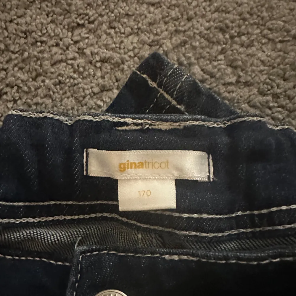 Snygga mörkblå jeans från Gina Tricot med bootcut-stil. De har framfickor med knappar och en bekväm passform. Perfekta för en avslappnad look.. Farkut & Housut.