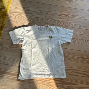 Vit t-shirt från Comme des Garçons - Säljer en stilren vit t-shirt från Comme des Garçons med guldigt hjärta. Storlek M men sitter som S/xs