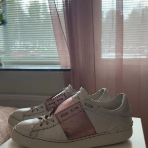 Valentino sneakers med rosa detaljer - Snygga Valentino sneakers i vitt med unika rosa detaljer. Skorna har snörning och en rund tå, vilket ger en klassisk men trendig look. Perfekta för att ge din outfit en lyxig touch. Skorna är i storlek 40 och är äkta, ganska använda men hela.