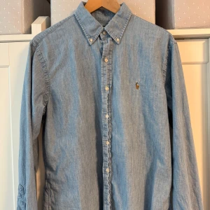 Polo Ralph Lauren skjorta  - Snygg blå skjorta från Ralph Lauren med klassisk krage och broderad logga på bröstet. Skjortan har knappar hela vägen och är perfekt för en stilren look. Skjortan är i stlk L, Slimfit model