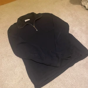 Marinblå långärmad tröja med dragkedja från East West - Säljer en stilren marinblå långärmad tröja från East West. Tröjan har en praktisk dragkedja vid halsen och en klassisk passform. Perfekt för en avslappnad look.