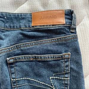Blå utsvängda, lågmidjade jeans  - Snygga blå jeans från Junkyard i storlek S. Klassisk femficksdesign med knapp och dragkedja framtill. Är köpta oanvända här från Plick och har bara testat dem, då de var för små. Skulle säga att den passar 34-36. Nypris 600!!