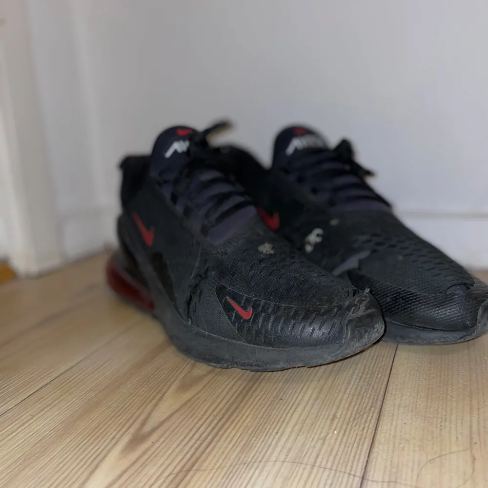 Säljer ett par svarta Nike Air Max 270 med röda detaljer. Skorna har en luftig design med snörning och en synlig Air-enhet i hälen för extra komfort. Lite hål vid tårna dock. Kengät.