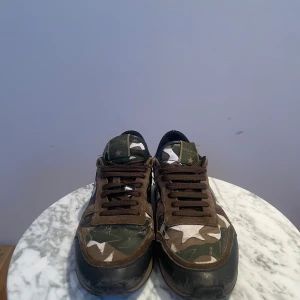 Valentino Rockrunner i camouflage - Snygga Valentino Rockrunner sneakers i ett coolt camouflagemönster med stjärndetaljer. Skorna har en kombination av gröna, bruna och svarta nyanser med en unik stjärna på hälen. Perfekta för att ge din outfit en edgy touch.