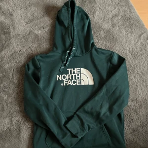Grön hoodie från The North Face - Säljer en snygg grön hoodie från The North Face med deras ikoniska logga i vitt på framsidan. Tröjan är St M men skulle mer säga passforms som S🤗 Tränings matrial på tröjan.