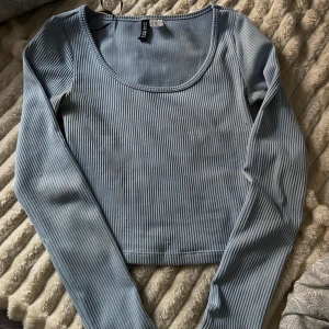 Ljusblå ribbad topp från H&M Divided - Säljer en ljusblå ribbad topp från H&M Divided. Toppen är croppad med långa ärmar och en rundad halsringning. Perfekt för en stilren och bekväm look. Passar som XS och en liten S.