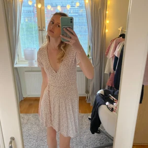 Ljuslila blommig kortklänning från Pull&Bear - Supersöt ljuslila kortklänning från Pull&Bear med blommigt mönster. Klänningen har v-ringning, korta ärmar och en lätt utställd kjol. Perfekt för vår och sommar, och ger en romantisk vibe med sitt mjuka material.