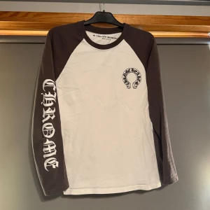Chrome Hearts långärmad tröja - Säljer en långärmad tröja från Chrome Hearts med vita och mörkgrå partier. Stora tryck på ryggen och ärmen samt mindre logga på bröstet. Tröjan har rund hals och är tillverkad i bomull. Helt perfekt skick kommer även strykas innan den skickas 😪