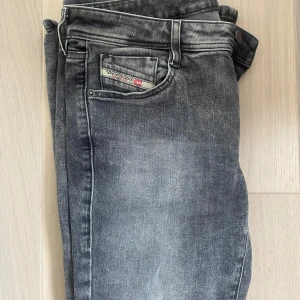 Diesel jeans - Säljer ett par grå bootcut jeans från Diesel med klassisk femficksdesign och diskret logga på myntfickan. Jeansen har en bootcut passform och låg midja, perfekta till vardags. Snyggt tvättad finish för en avslappnad look. Passar S-M.