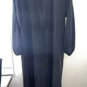 Svart Abaya - En svart abaya med rund halsringning och hel dragkedja framtill. Abaya har långa ärmar med lätt puff och är tillverkad i ett mjukt, slätt material. Enkel och stilren design som passar till många tillfällen.  Den är helt ny och aldrig använd. Prislappen är inte kvar men plastet från lappen är kvar. 