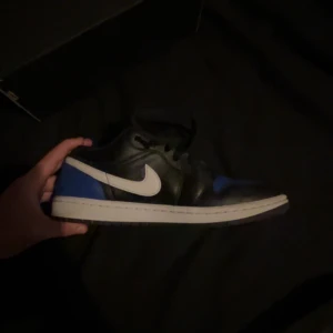 Nike Air Jordan 1 Low svart/blå - Säljer ett par använda  Nike Air Jordan 1 Low i svart och blått med vit swoosh. Skorna har klassisk låg siluett, snörning och platt sula. Perfekta för dig som gillar streetwear och vill ha en ikonisk sneaker i garderoben. Kan mötas upp eller så addar ni snap o fortsätter därifrån 