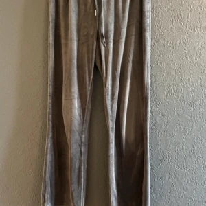 Grå mjukisbyxor i velour från Gina Tricot - Gråa mjukisbyxor i mjuk velour från Gina Tricot. Byxorna har resår och snörning i midjan för extra komfort. Perfekta för en avslappnad stil och tillverkade i polyesterblandning.