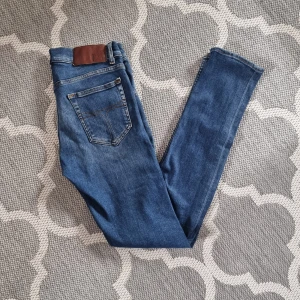 Blå slim jeans med klassisk femficksdesign - Säljer ett par blå slim fit jeans med klassisk femficksdesign och snygga kontrastsömmar. Jeansen har normal midja och raka ben, tillverkade i jeansmaterial. Passar perfekt till vardagslooken.