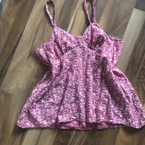 Rosa blommig sommartopp☀️ - Söt rosa topp med små vita blommor och smala axelband. Toppen har en lätt utställd passform och v-ringad överdel. Perfekt för varma dagar och har en luftig känsla. Tyget har lite glitter som strålar fint i solen☀️