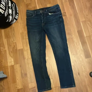 Mörkblå slim tapered jeans Ethan - Snygga mörkblå jeans i modellen slim tapered från Ethan. Klassisk femficksdesign med smal passform upptill och avsmalnande ben. Jeansen har dragkedjegylf och kontrastsömmar. Perfekta för en stilren vardagslook.