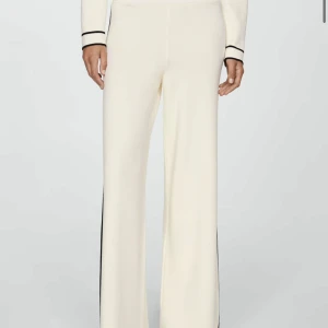 Vita vida byxor från Mango - Snygga vita byxor med vida ben och svarta ränder längs sidorna. Byxorna har en hög midja och är tillverkade i ett stickat material som känns mjukt och bekvämt. Perfekta för en stilren och trendig look. NYPRIS 600kr!! Storlek M🥰