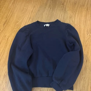 Mörkblå sweatshirt med puffärmar - Säljer en mörkblå sweatshirt med puffiga ärmar och rund hals. Tröjan har en enkel design och bred mudd vid ärmslut och nederkant. Perfekt för en avslappnad stil.