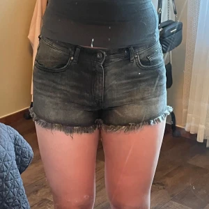 Svarta jeansshorts med fransar - Snygga svarta jeansshorts med råa fransade kanter och klassisk femficksdesign. Shortsen har normal passform och låg midja, perfekta för sommardagar. Stilrena och lätta att matcha med olika toppar.