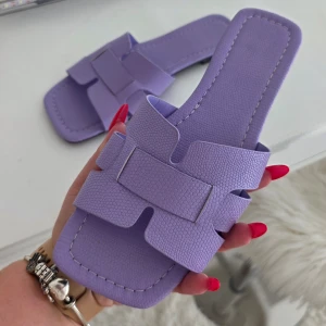 Lila sandaler med breda remmar - Säljer ett par trendiga lila sandaler med breda, korsade remmar och fyrkantig tå. Skorna har en platt sula och är tillverkade i ett syntetmaterial med lätt textur. Perfekta för varma dagar och enkel att matcha med sommarens outfits.