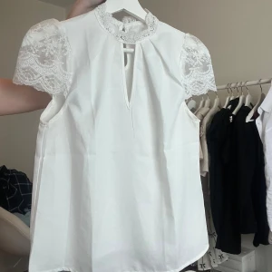 Vit blus med spetsdetaljer - Säljer en elegant vit blus med spets på ärmarna och runt kragen. Riktigt fin och passar för alla tillfällen, endast använd enstaka gång.💕