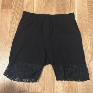 Svarta shorts med spets från Lindex - Svarta shorts från Lindex med bred resår i midjan och fina spetsdetaljer längst ner på benen. Mjukt och stretchigt material som sitter bekvämt. Perfekta för en stilren och feminin look.