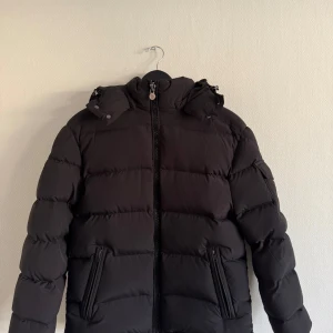 Moncler montgenevre - Säljer en svart dunjacka från Moncler med huva och dragkedja framtill. Jackan har två snedställda fickor med dragkedja. Storlek 3 vilket motsvarar ungefär M. Finns även med väska till jackan . Eftersom man bara kan lägga ut 5 bilder så får ni gärna fråga om fler om så önskas 