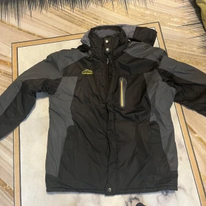 Svart och grå outdoorjacka med fleecefoder - Säljer en svart och grå outdoorjacka från Outdoor Jackets. Jackan har mjukt grått fleecefoder, huva och dragkedja framtill samt en bröstficka med dragkedja. Perfekt för kyliga dagar och outdoor-aktiviteter.  Storleken är XL !!!