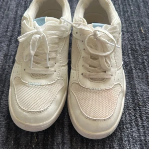 Vita sneakers från ONLY - Säljer ett par vita sneakers från ONLY med meshdetaljer och snörning. Skorna har en platt sula och ljusblå detalj på hälen. Perfekta för en clean och sportig look.
