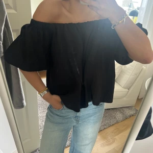 Svart offshoulder blus - Säljer en svart offshoulder blus med vida ärmar. Toppen har en lös passform och resår vid axlarna för en snygg och bekväm look. Perfekt att styla med jeans eller kjol.