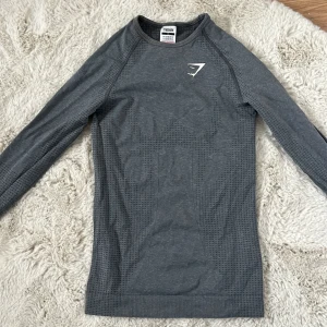 Grå långärmad träningströja från Gymshark - Säljer en grå långärmad träningströja från Gymshark med diskret mönster och tumhål vid ärmsluten. Perfekt för gymmet eller löpning. Tröjan har en tight passform och är tillverkad i ett syntetmaterial som andas. Supercute! Skriv vid frågor eller funderingar!😝🫰😅❤️