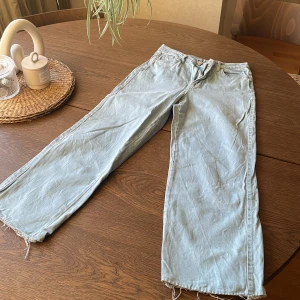 Ljusblåa jeansbyxor från Madlady - Säljer ett par ljusblåa jeansbyxor från Madlady med raka, vida ben och råa kanter nertill. Klassisk femficksmodell och hög midja. Perfekta för en avslappnad och trendig look.