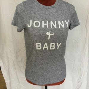Grå T-shirt River Island Strl: 8 - Gråmelerad t-shirt från River Island med vitt tryck där det står 'JOHNNY & BABY' på framsidan. Klassisk passform och rund halsringning. Perfekt för en avslappnad stil. T-shirt med tryck Saknar tvättråd  Uppskattat material: bomullsblandning Katter finns i hemmet!