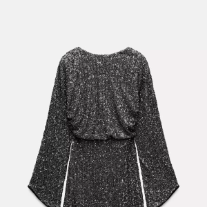 Glittrig svart kortklänning med långa ärmar - Säljer en snygg svart glittrig kortklänning med långa ärmar och rund hals. Klänningen har en figurnära passform upptill och markerad midja. Perfekt för dig som vill sticka ut på festen!