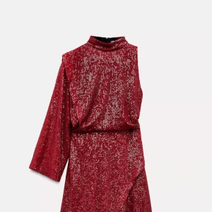 Röd glittrig kortklänning med asymmetrisk ärm - Säljer en röd glittrig kortklänning med hög krage och en lång ärm. Klänningen har en unik asymmetrisk design och en lätt omlott-effekt framtill. Perfekt för dig som vill sticka ut med en trendig look.