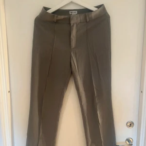 gråa kostymbyxor från Madlady - Säljer ett par stilrena gråa kostymbyxor från Madlady i storlek EU36. Byxorna har pressveck framtill, bälteshällor och stängs med dragkedja. super fina!! 