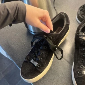 Svarta sneakers från Steve Madden i sammet - Säljer ett par svarta sneakers från Steve Madden i mjuk sammet och svarta satin band. Skorna har vit sula och metallplatta med logga. 