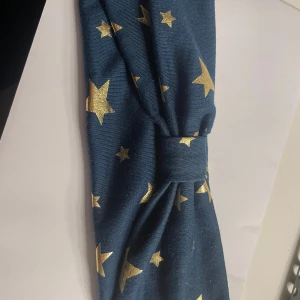 Blått diadem med guldstjärnor - Snyggt blått diadem med glittriga guldstjärnor. Diademet har en knut framtill som ger en trendig look. Perfekt accessoar för att piffa upp din outfit.