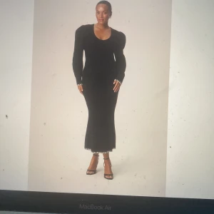 Svart långklänning från Adoore - Säljer en svart långklänning från Adoore med lång ärm och rund halsringning. Klänningen har ribbad struktur och dekorativa detaljer vid ärmslut och nederkant. Perfekt för dig som gillar stilrena och eleganta plagg.