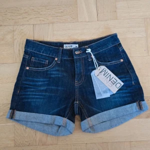 Mörkblå jeansshorts med uppvik - Snygga helt ny med taggen kvar mörkblå jeansshorts från Denim med klassisk femficksdesign och uppvikta benslut. Shortsen har orangea kontrastsömmar och bälteshällor, perfekta för sommardagar.