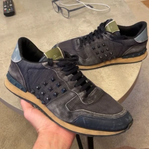 Valentino Rockrunner - Säljer ett par Valentino Rockrunner sneakers i mörkblått med svarta nitar på sidorna. Skorna har svarta snören, beige sula och detaljer i mocka och skinn. Klassisk rund tå och platt sula. Perfekta för dig som gillar streetstyle. Priset kan diskuteras vid snabb affär, kvitto ingår och vill bara bli av med de. Äkta såklart!