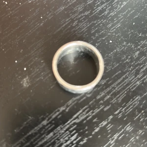 Silverfärgad ring med snirkligt mönster - Säljer en stilren silverfärgad ring med ett snirkligt mönster runt om. Perfekt accessoar för dig som gillar unika detaljer. Ringen är bred och har en matt finish. Plus den är ganska stor.