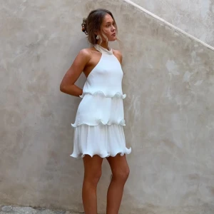 Vit volangklänning med halterneck - Säljer en superfin vit kortklänning med halterneck och flera volanglager. Klänningen knyts i nacken och har en luftig, flowy passform som känns både trendig och romantisk. Perfekt studenten (helt ny)