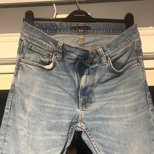 Ljusblå jeans från Nudie Jeans - Säljer ett par klassiska ljusblå jeans från Nudie Jeans med snygga kontrastsömmar och ikonisk brodyr på bakfickorna. Modellen har fyra fickor, normal passform och raka ben. Perfekta till sneakers eller boots för en chill look. Storlek är W29 och L34