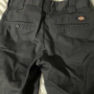 Svarta Dickies byxor W30/L30 - Svarta byxor från Dickies med klassisk look och raka ben. Byxorna har två bakfickor med knapp och Dickies-logga ovanför ena fickan. Tillverkade i slitstarkt material, perfekta för en clean och stilren vibe.