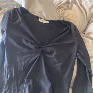 Svart långärmad topp från Kappahl - Svart långärmad topp från Kappahl i mjuk bomull. Toppen har en snygg v-ringning med twistad detalj framtill som ger en cool look. Perfekt att styla med jeans eller kjol för en trendig outfit.