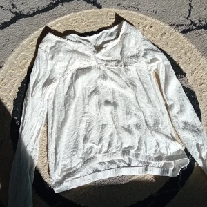 Vit blus med spetsdetaljer - Säljer en söt vit blus med lång ärm och fina spetsdetaljer upptill. Blusen har v-ringning och ett lätt strukturerat tyg med diskret mönster. Perfekt för dig som gillar romantisk och feminin stil.