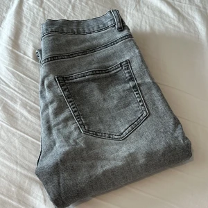 Grå jeans från Lindex, rak modell - Snygga grå jeans från Lindex i rak passform. Klassisk femficksmodell med bälteshällor och knappstängning. Jeansen har en tvättad look och är tillverkade i mjuk bomullsdenim. Perfekta för dig som gillar en enkel och stilren vibe. Väldigt bra skick. Hör av er om frågor eller prisförslag.